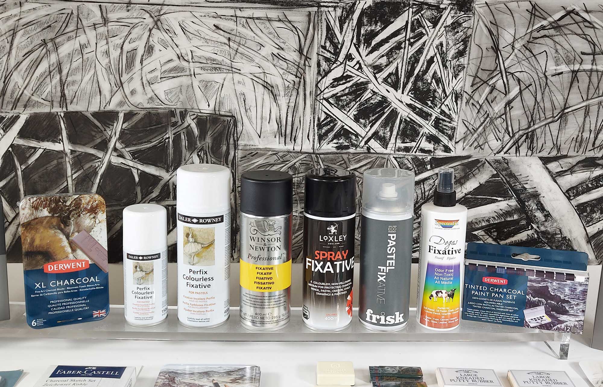 Spray fixative brands lined up in front of a large Black and White Charcoal study.
