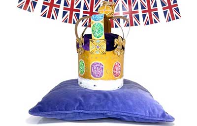 Gold bejewelled paper crown sat on top of a purple cushion.