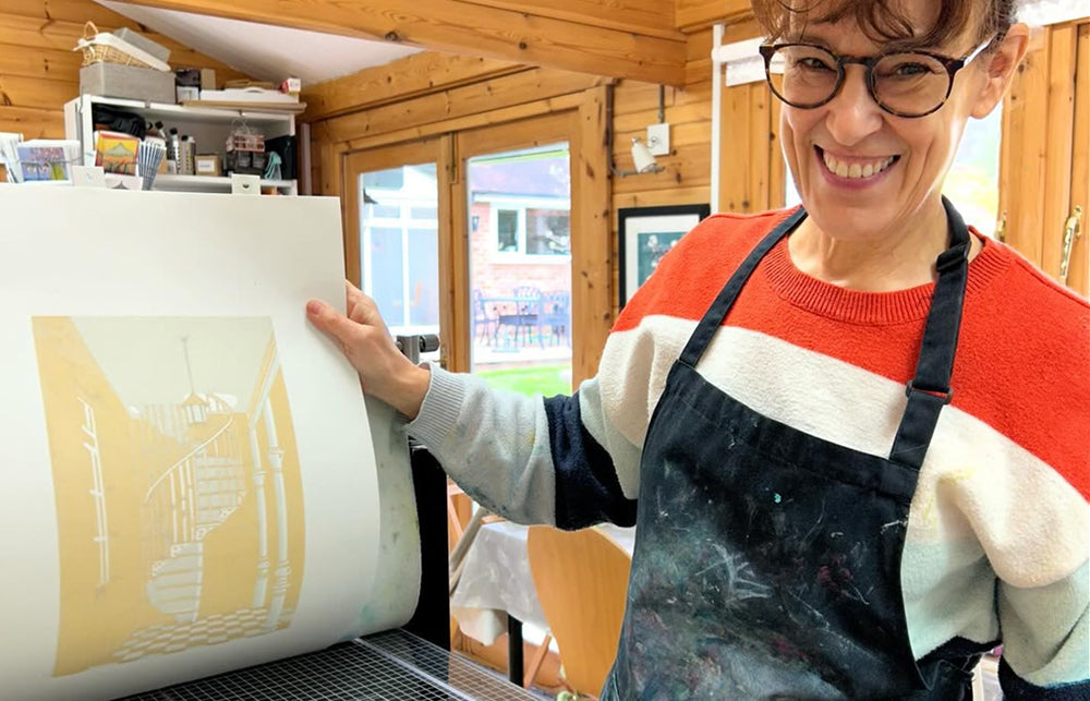 Print artist Nathalie Pymm stood in front of her printing press holding up a print.