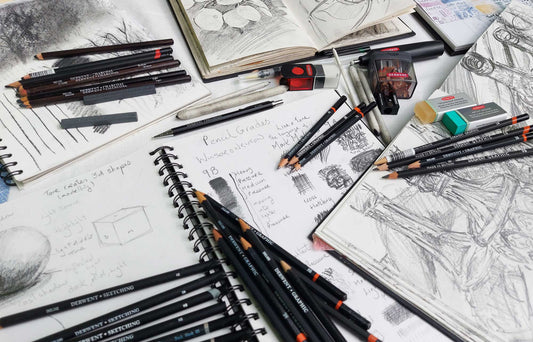Open sketchbooks with drawings studies and drawings of bottles by Ellie Jakeman. Derwent Graphic pencils scattered over the pages.