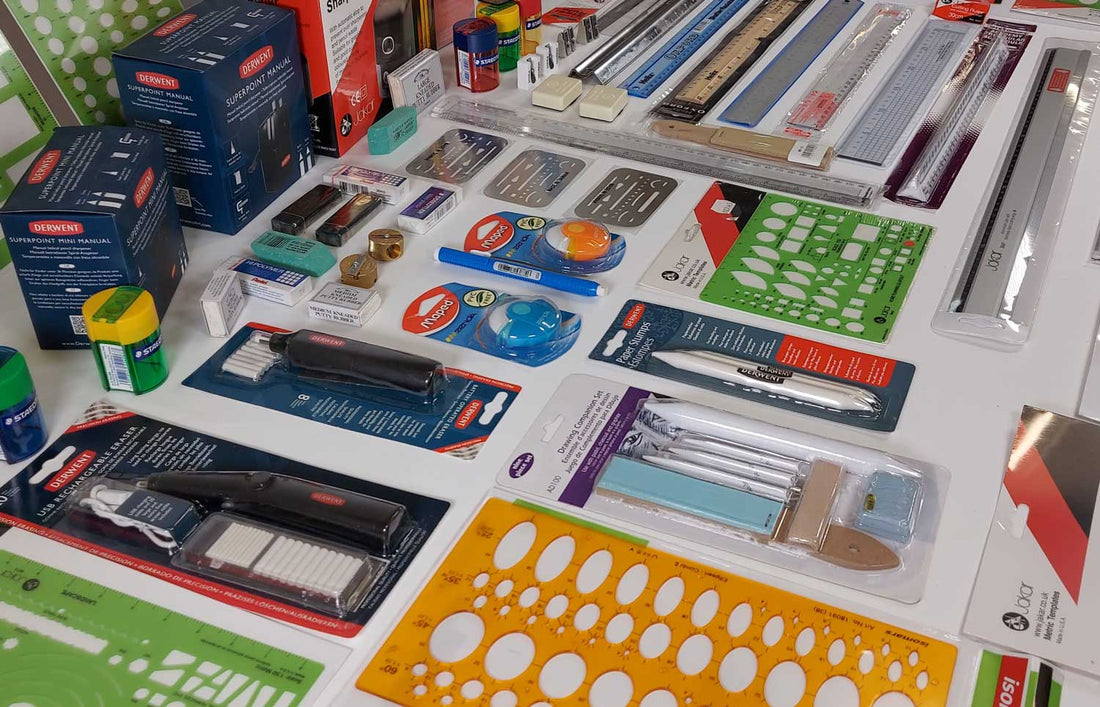 Multiple products for artists laid flat in rows on a white desk, erasers, stencils, paper stumps, rulers, and sharpeners. 