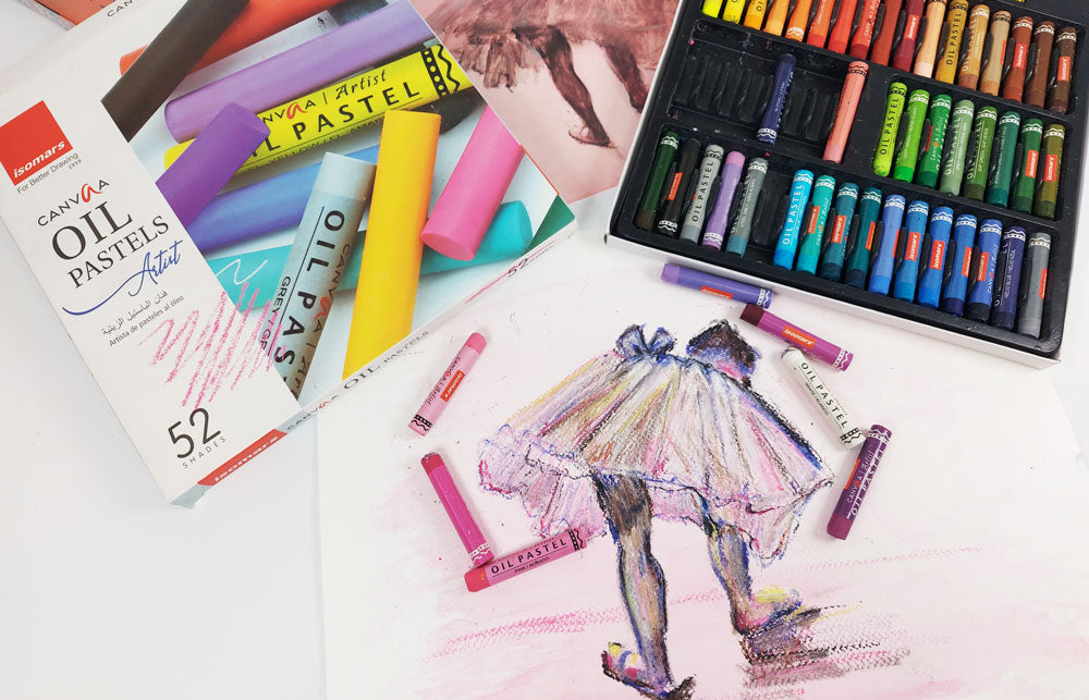 Set of of Isomars canva oil pastels set out on a desk with a drawing of a ballet dancer.