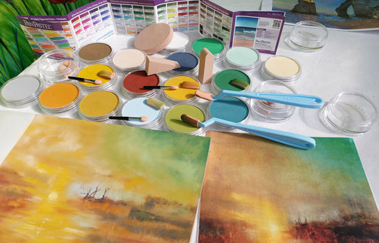 Pan Pastel warm colours set out on a desk with Sofft sponge applicators in front of a pastel painting of a landscape. 