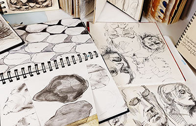 Open sketchbooks with black and white pencil and pen drawings of faces and shells.