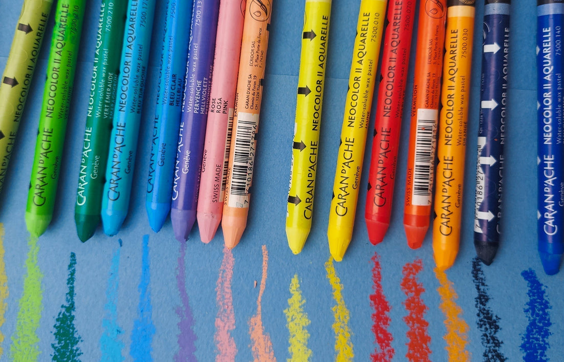 Multiple Caran D'Ache Neocolor II Aquarelle Water-soluble wax pastels set on top of a blue paper