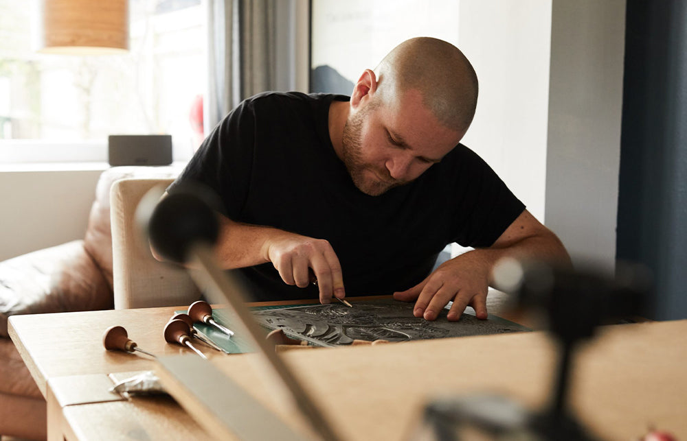 Andrew Campe print artist sat at a desk cutting into a  piece of lino in preparation for a print.