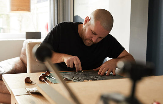 Andrew Campe print artist sat at a desk cutting into a  piece of lino in preparation for a print.
