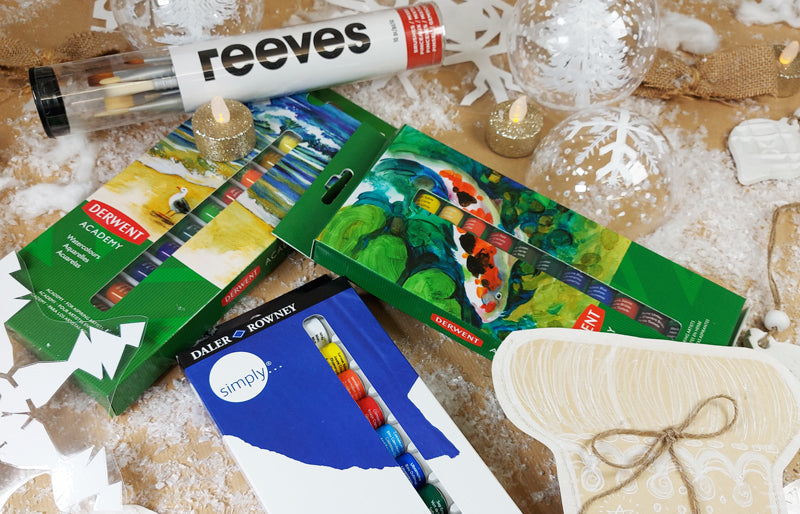 Derwent tubes of watercolour in their original boxes scattered on a table surrounded by Christmas decorations.