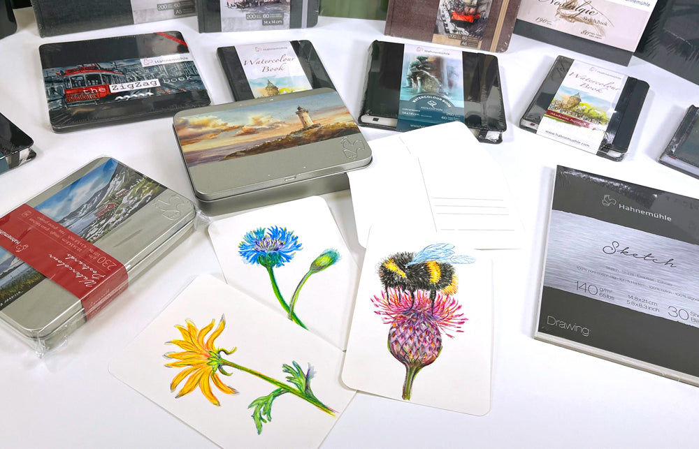 Painted Bee sitting on top of a clover blossom created on Hahnemuhle post card watercolour paper, surrounded by Hahnemuhle postcard tins 