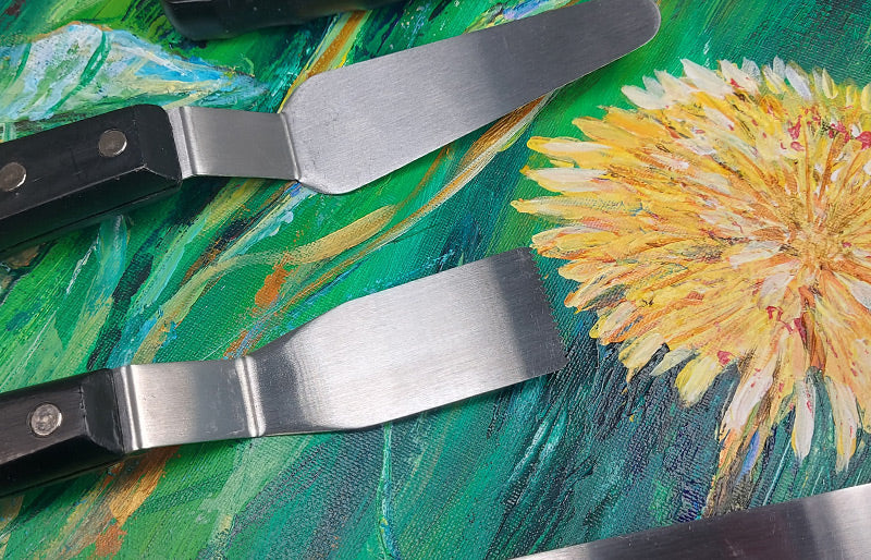Liquitex palette knives resting on a vividly painted canvas of Dandelion heads. 