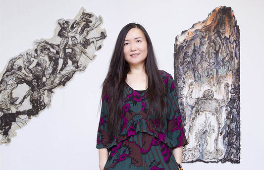 Artist Yin Wang stood in front of two pieces of artwork.