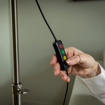 Hand holding a control device with red, green, and yellow buttons near a metal pole.