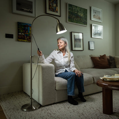 Woman sitting on a couch in a living room adjusting a floor lamp.