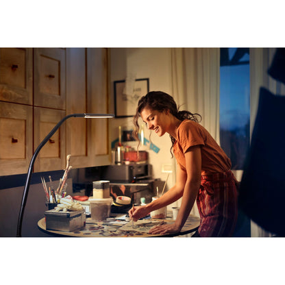 Woman working at a table illuminated by Daylight Company Electra Floor Lamp, focusing on her artwork.